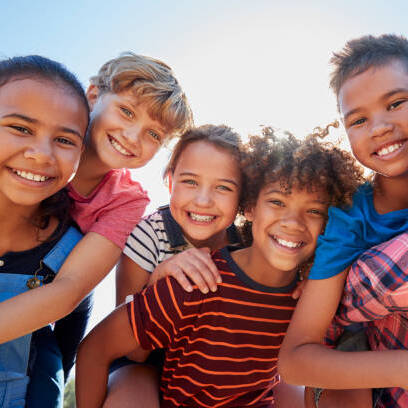 Six pre-teen friends piggybacking in a park, close up portrait